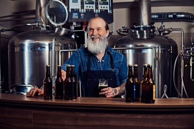 Çelik varillerin etrafındaki neşeli yaşlı adam içerde bira fabrikasında.