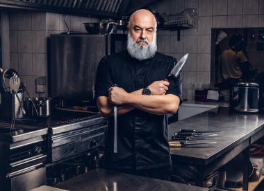 Mutfakta mutfak aletleri tutan gri saçlı şef.