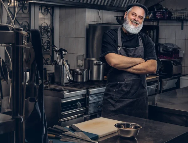 Chef idoso alegre com avental e boné posando com braços cruzados — Fotografia de Stock