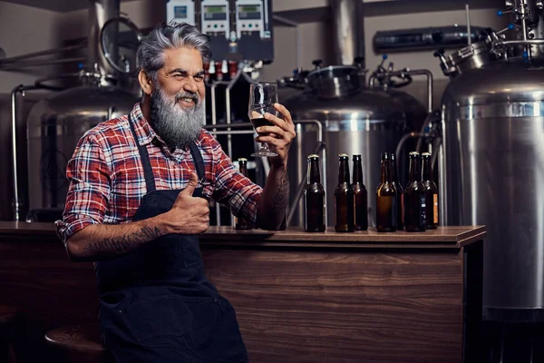Joyful velho cervejeiro mostrando polegares para cima degustando sua cerveja — Fotografia de Stock