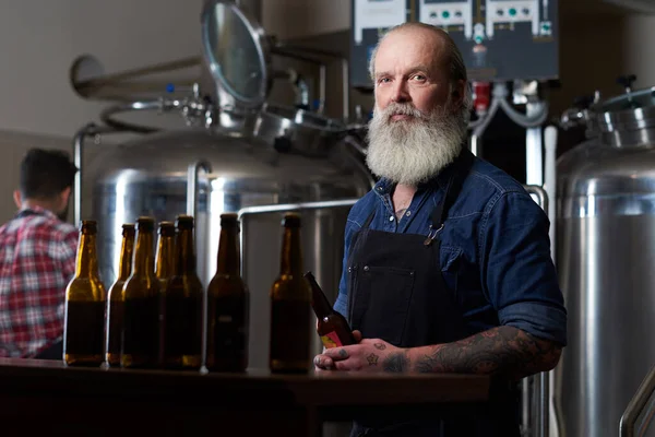 Oudere man rond tafel met bierflesjes in bierfabriek — Stockfoto