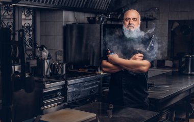 Yaşlı kel şef mutfağında tüttürüyor.