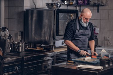 Yaşlı aşçı restoranın mutfağında yemek pişiriyor.