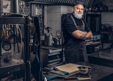 Önlüklü, şapkalı, kolları çapraz duran kendinden emin yaşlı bir aşçı.