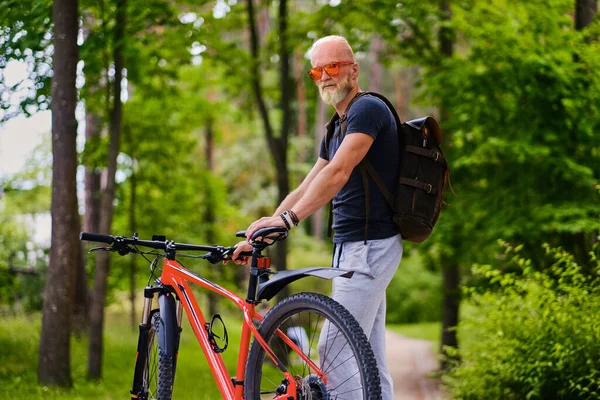 Bisikletli ve sırt çantalı sportif yaşlı bir bisikletçi. — Stok fotoğraf