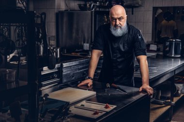 Önlük giymiş yaşlı ve mutfakta siyah giysili ciddi bir aşçı.