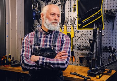 Ekose gömlek ve atölyede tulum giymiş yaşlı bir tamirci.