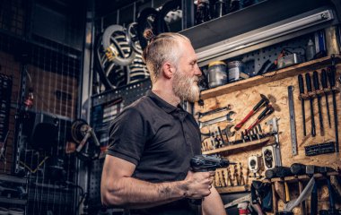 Atölyedeki tezgahın etrafında matkapla yaşlı bir zanaatkar.