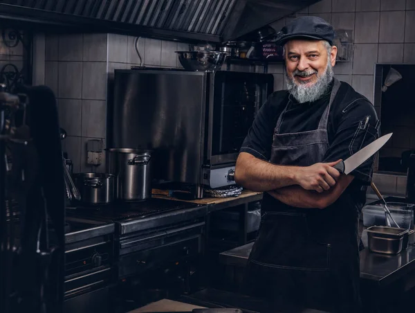 Joyeux vieil homme chef tenant couteau dans la cuisine moderne — Photo