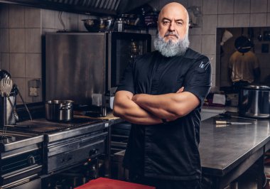 Mutfakta siyah giysili gri saçlı şef.