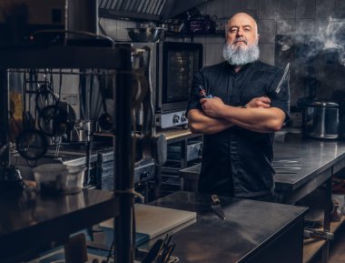 Yaşlı kel şef mutfağında tüttürüyor.