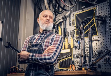 Tamircide İngiliz anahtarı tutan gri sakallı yaşlı bir tamirci.