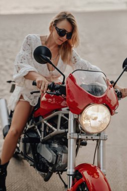 Gün batımında plajda motorsikletli havalı bir kadın.