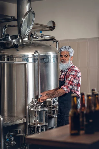 Anciano vestido de delantal trabajando en una cervecería moderna — Foto de Stock