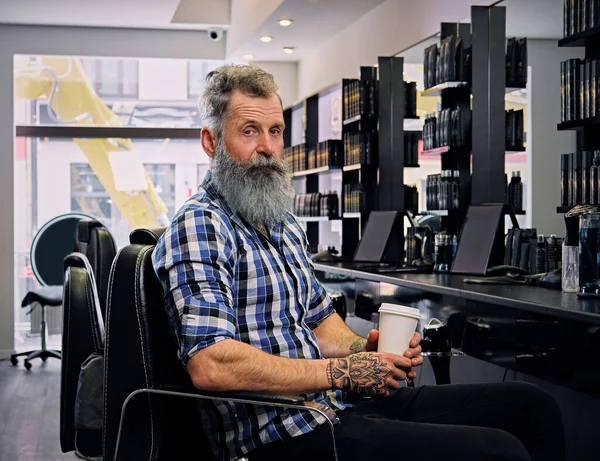 Getatoeëerde oude man hipster met koffie in moderne kapsalon — Stockfoto