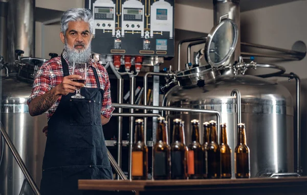 Старий пивовар позує в пивоварні навколо столу є пляшки пива — стокове фото