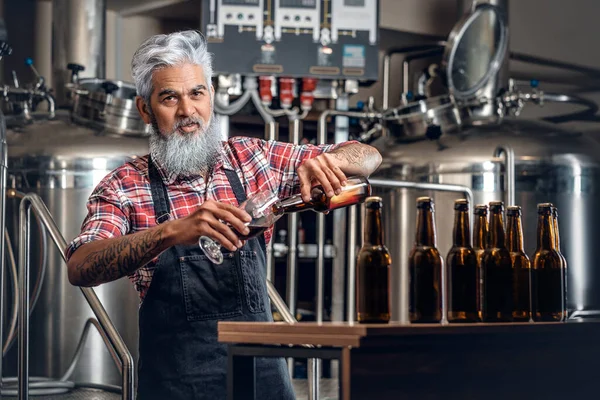 Старий наповнює пиво склянкою в сучасній броварні — стокове фото