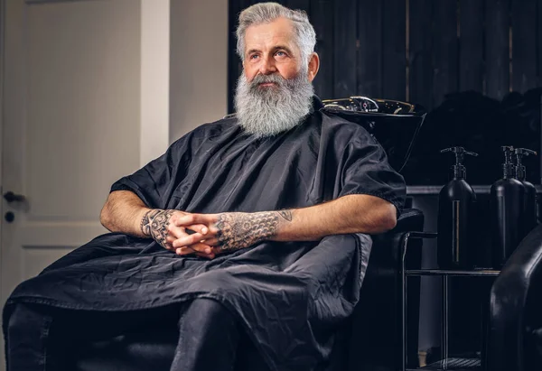 Модний старий хіпстер з піньйором і довгою бородою в перукарні — стокове фото