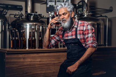 Bira fabrikasında bira içen önlük giymiş yaşlı bir bira üreticisi.