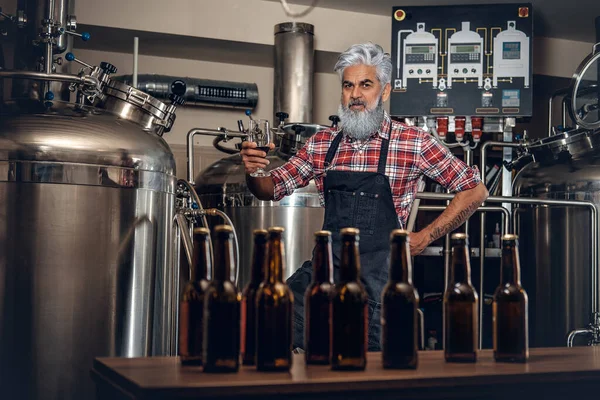 Bira fabrikasında poz veren eski bira üreticisi. Bira şişeleri var. — Stok fotoğraf