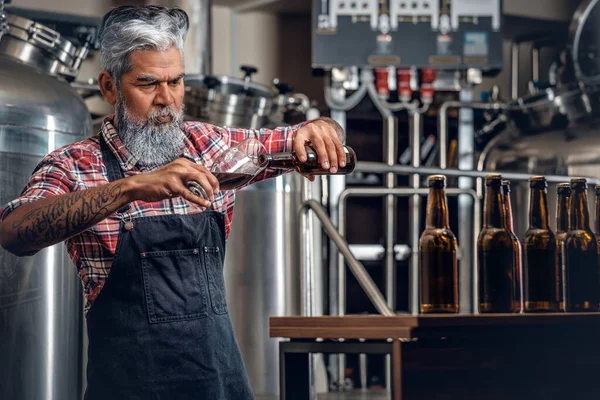 Alter Mann gießt in moderner Brauerei Bier ins Glas — Stockfoto