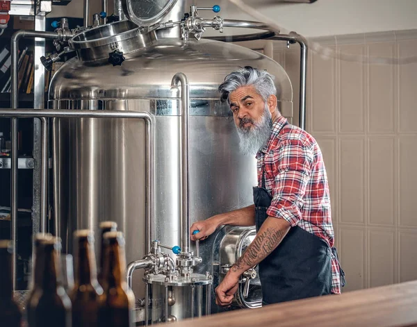 Старий, одягнений у фартух, працює в сучасній пивоварні — стокове фото