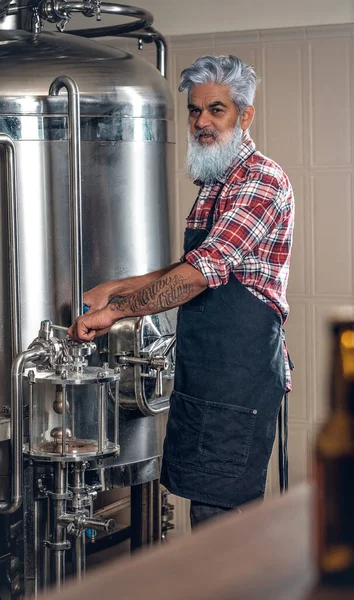 Старий, одягнений у фартух, працює в сучасній пивоварні — стокове фото