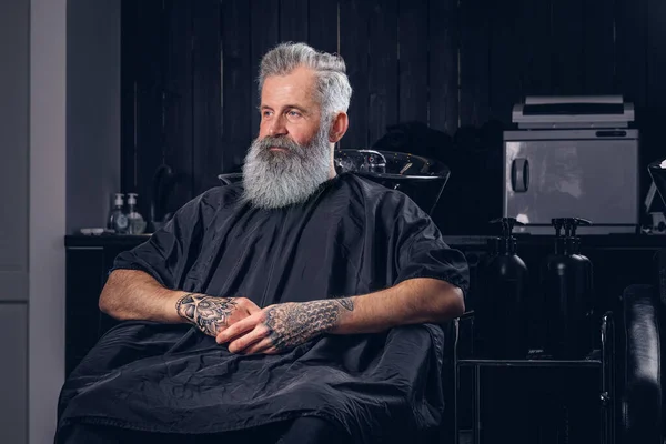Hipster velho na moda com peignoir e barba longa na barbearia — Fotografia de Stock