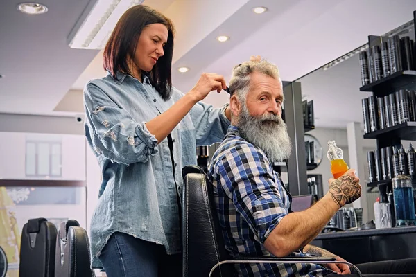 Kvinnelig hårstylist klipper hår på eldre hipster med juice – stockfoto