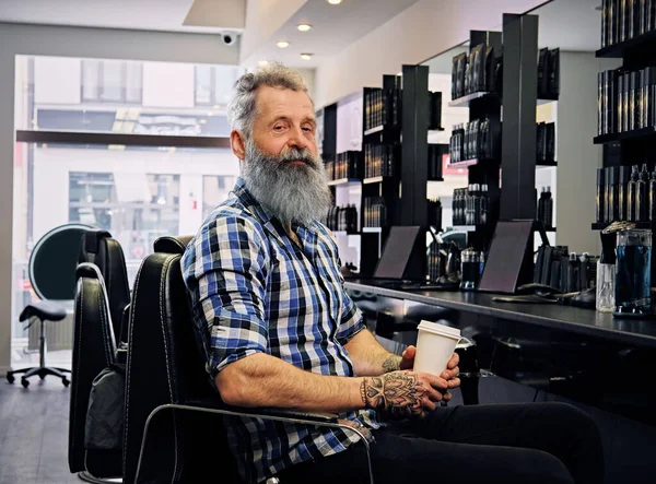 Tatuado velho hipster com café no salão de cabeleireiro moderno — Fotografia de Stock