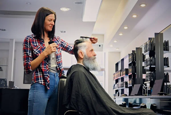 Mulher alegre cortando seu cliente velho na barbearia — Fotografia de Stock