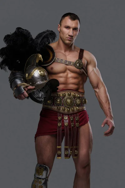 Gladiator with muscular build holding helmet against gray background — Fotografia de Stock