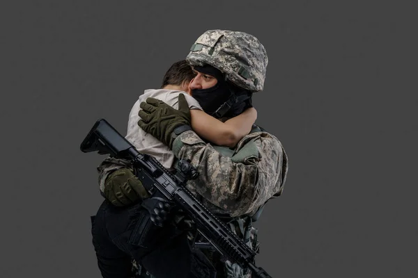 Special force soldat kramar liten unge mot grå bakgrund — Stockfoto