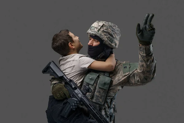 Special force soldier carrying little boy against gray background — Fotografia de Stock