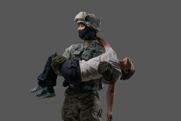 Modig soldat patriot som bär skadade barn mot grå bakgrund — Stockfoto