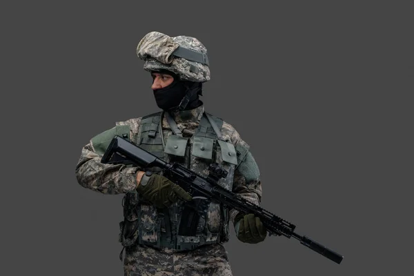 Modern serviceman with rifle posing against gray background — Stock Photo, Image