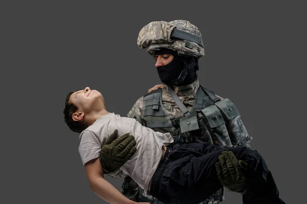 Homme militaire portant enfant blessé isolé sur fond gris — Photo