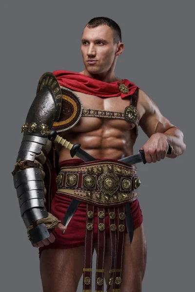 Muscular colosseum fighter holding twin swords against grey background — Stock fotografie