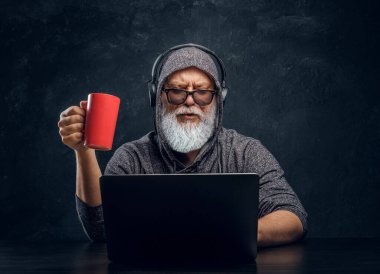 Şık büyükbaba bilgisayar kullanarak kulaklık ve fincanla hackerlık yapıyor.