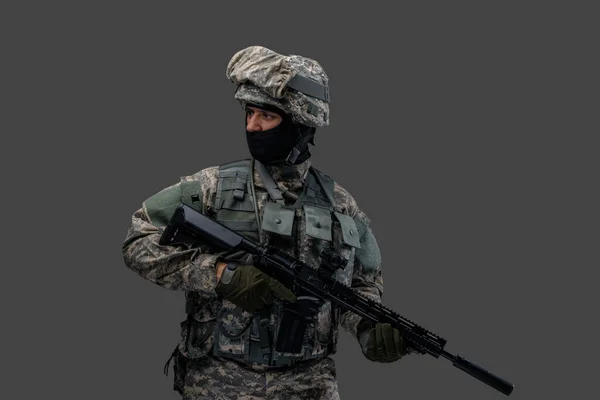 Modern serviceman med gevär poserar mot grå bakgrund — Stockfoto