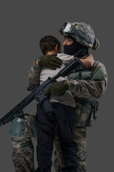 Gri arka planda izole edilmiş küçük çocuğu kucaklayan bir asker. — Stok fotoğraf