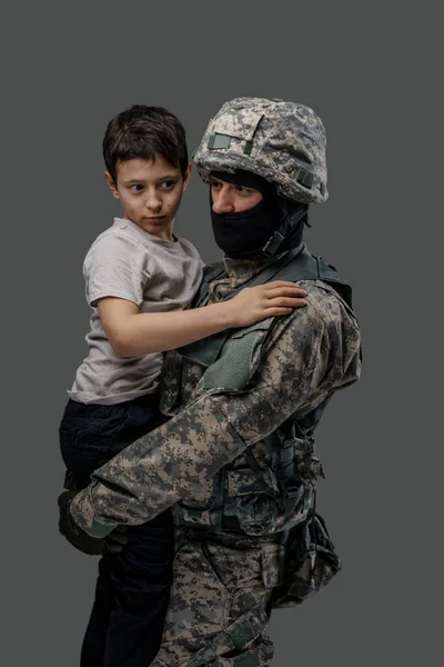 Soldat de la force spéciale serrant petit enfant dans ses bras sur fond gris — Photo