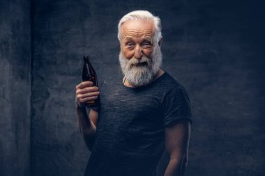 Şişeli neşeli yaşlı adam karanlık arka planda poz veriyor.