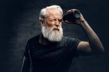 Modern saç stili olan yaşlı adam şişeden bakıyor.