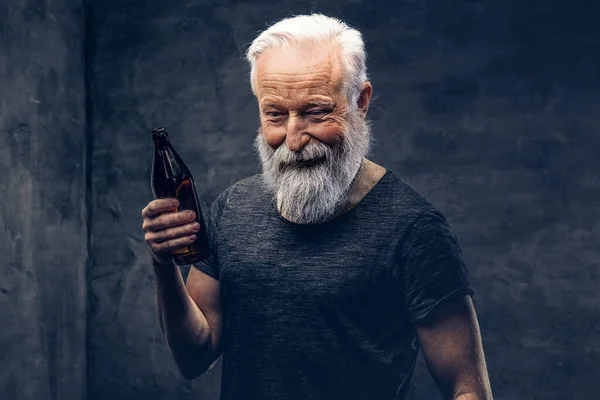 Joyful old man with bottle posing against dark background — Photo