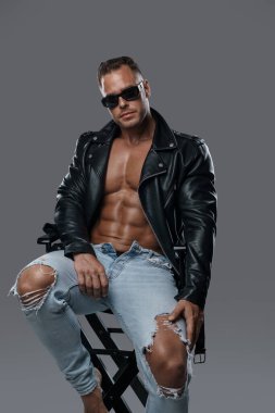 Şık giyinmiş kaslı adam sandalyede oturuyor.