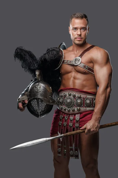 Muscular gladiator spearman with helmet against grey background — стоковое фото