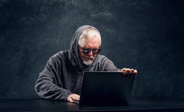 Karanlık arka planda dizüstü bilgisayarı olan yaşlı hacker.