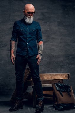 Karanlık arka planda dövmeleri olan şık, yaşlı bir hippi.