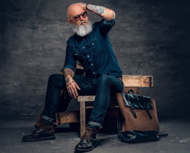 Trendy senior man with tattooes sitting on wood